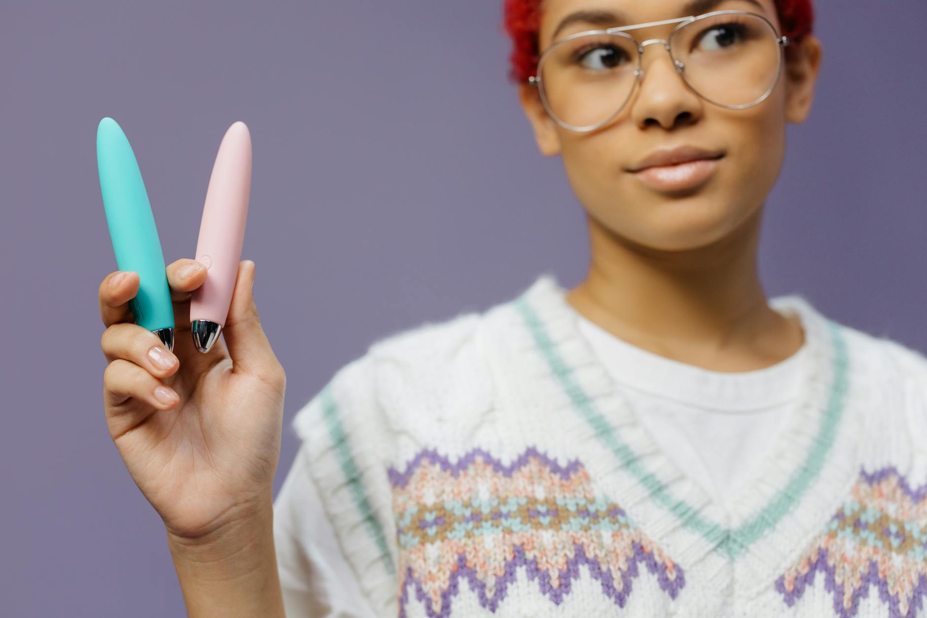 A woman holding colorful vibrators against a purple background, exploring different sensations